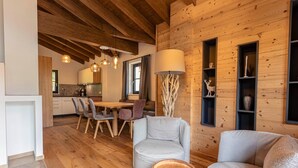 Un intérieur moderne avec des murs en bois, un coin repas avec une table et des chaises, et un espace détente avec une lampe et des étagères.