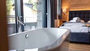 Une salle de bain moderne avec une baignoire sur pieds, un plancher en bois et un lit recouvert de linge de maison blanc, soigneusement disposé.