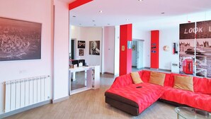 Un moderno cuarto de hotel con un sofá rojo, una mesita pequeña y un cuadro grande en la pared.