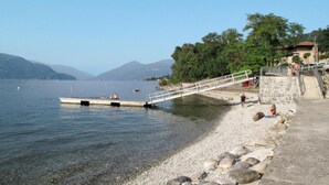 Una playa junto al lago con un muelle que se adentra en el agua, una escalera de piedra que baja hacia la orilla y una vista despejada de las montañas circundantes.
