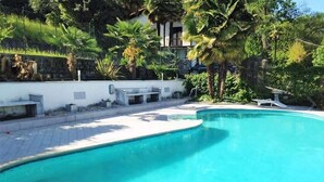 Una piscina de borde curvo, rodeada por una terraza de baldosas blancas.