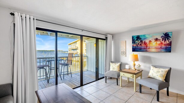 A room with a view of the sea, a balcony with chairs, a table, and a painting of a sunset. - Gulf front condo with sunset views (Cedar Key)