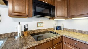 A kitchen with wooden cabinets, a black microwave, a granite countertop, a stainless steel sink, and a sign that reads "Sandy Toes and Sally Kisses." - Gulf front condo with sunset views (Cedar Key)