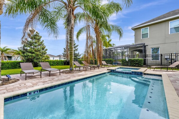 A swimming pool with lounge chairs, palm trees, and a house in the background.