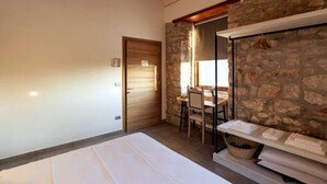 A bedroom with a bed, a wooden door, a stone wall, a table with chairs, and a hanging rack. - Tenuta San Martino - Irpinia (Nusco)