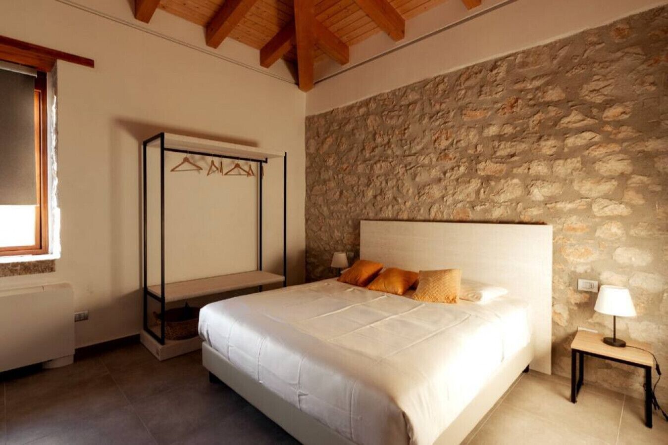 Un dormitorio con pared de piedra, cama con ropa de cama blanca y techo de madera.