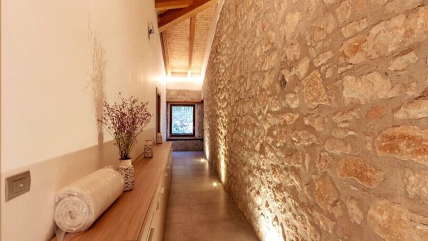 A hallway with stone walls, a wooden bench with a rolled towel, and a vase with dried flowers. - Tenuta San Martino - Irpinia (Nusco)