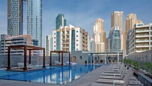 A rooftop swimming pool with lounge chairs and a pergola, surrounded by high-rise buildings. - Cozy 1BR with balcony sea view (Dubai)
