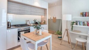 A modern kitchen with white cabinets, a wooden countertop, and a dining area with a table and chairs. - Cozy 1BR with balcony sea view (Dubai)