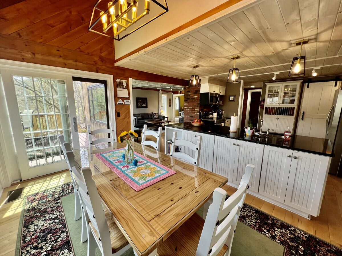 Une cuisine spacieuse avec des meubles blancs, une table à manger en bois et une vue sur l’extérieur grâce à de grandes fenêtres.