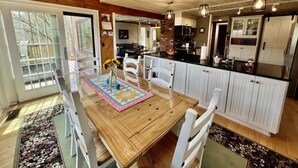 Una cocina amplia con armarios blancos, una mesa de comedor de madera y vistas al exterior a través de ventanas grandes.