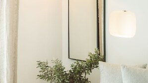 A modern room with a minimalist design, featuring a large mirror, two pendant lights, a wooden side table with a plant, and a light-colored sofa. - K-Log Studios  (Kas)