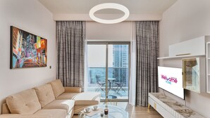 A modern living room with a sofa, a glass coffee table, a flat-screen TV, and a balcony with a table and chairs. - 1BR view in a luxurious home (Dubai)