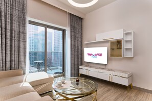 A modern living room with a large TV, a glass coffee table, a sofa, and a balcony with a view of high-rise buildings.