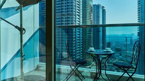 A balcony with a glass wall, a table with chairs, and a large umbrella. - 1BR view in a luxurious home (Dubai)