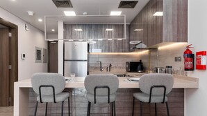 A modern kitchen with a central island, bar stools, and a fire extinguisher on the wall. - 1BR view in a luxurious home (Dubai)