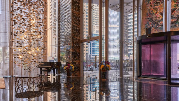 A modern lobby with a reflective floor, a grand piano, and large windows offering city views. - 1BR view in a luxurious home (Dubai)