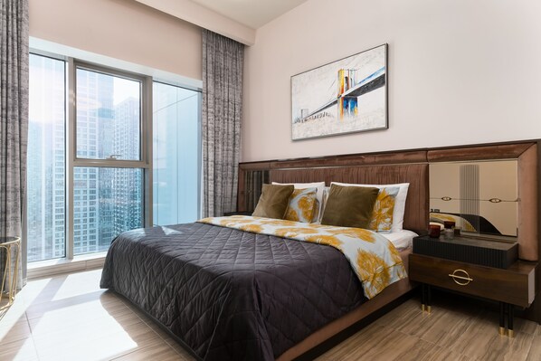 A modern bedroom with a large bed, a nightstand, a mirror, and a city view through large windows.