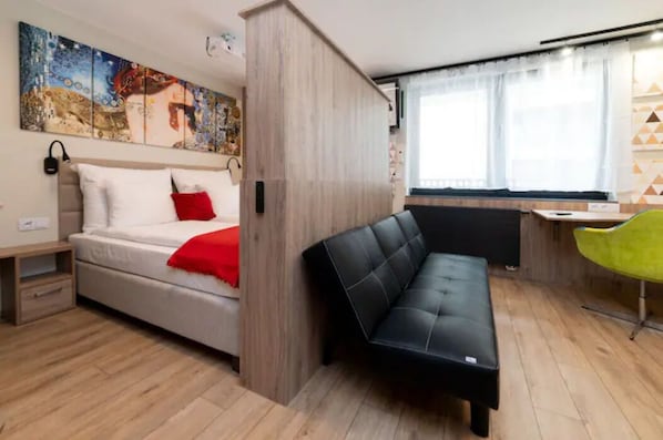 A compact room with a bed, a black sofa, a desk, and a chair.