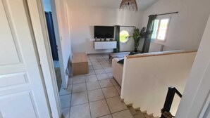 Ein geräumiger Wohnbereich mit Fernseher, einer Holzbank und einer Hängeleuchte.
