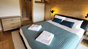 Un dormitorio con cama, mesita de noche, armario de madera, ducha y estante fijado a la pared.