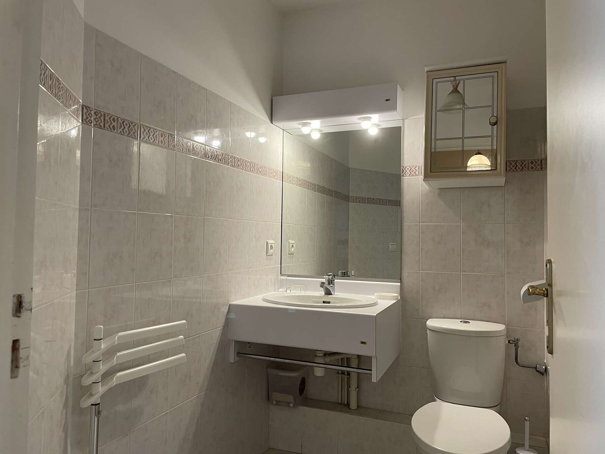 A bathroom with a white sink, mirror, and toilet, tiled walls, and a towel rack.