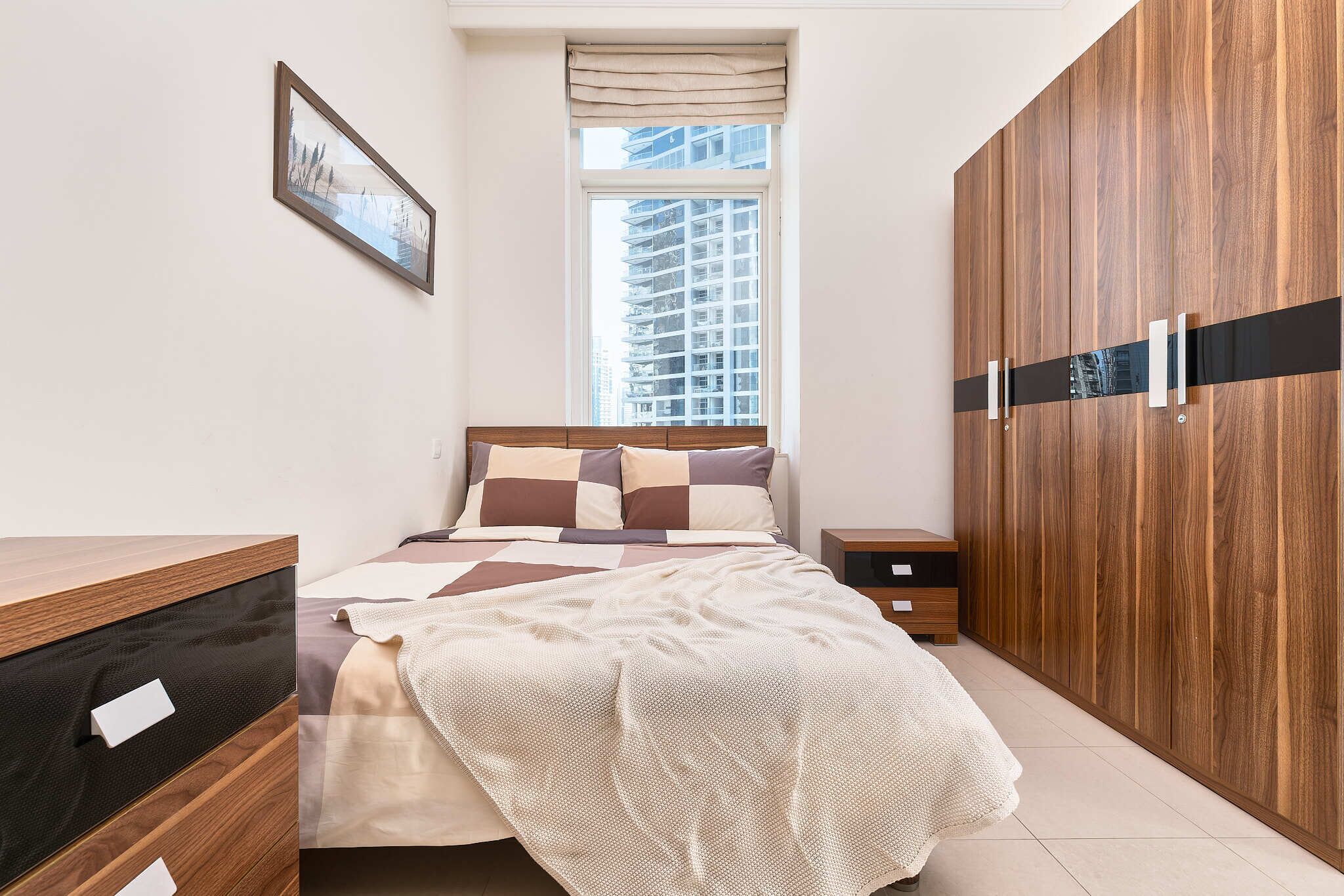 Ein Schlafzimmer mit Bett, Holzschrank, Nachttischen und einem Fenster mit Blick auf Gebäude.