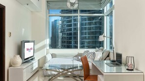 A modern hotel room with a bed, a desk with a laptop, a TV, and a large window with a city view. - Beautiful 1BR with sunset view (Dubai)
