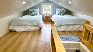 Un pequeño y acogedor dormitorio en el ático con dos camas, un banco de madera y una ventana decorada con una estrella de mar.