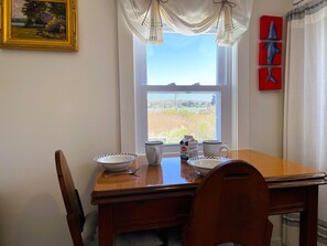 A dining table with a window view, a framed painting, and three shark sculptures on the wall. - Seaside Escape-Art-filled 2 Bd on Town Cove (EASTHAM)