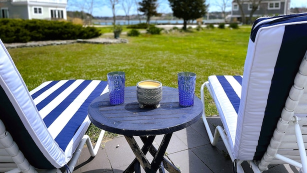 Un patio con dos sillones reclinables a rayas, una mesita redonda y dos portavelas de vidrio azul.