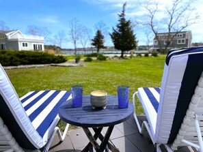A patio with two striped lounge chairs, a small round table, and two blue glass candle holders. - Seaside Escape-Art-filled 2 Bd on Town Cove (EASTHAM)
