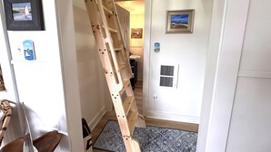 Una escalera estrecha que conduce a una plataforma con una puerta, una alfombra pequeña y cuadros en las paredes.