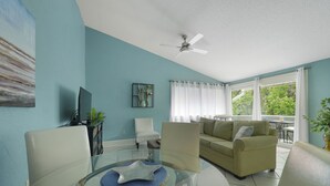 A living room with a glass dining table, a sofa, and a ceiling fan.