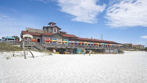 A beachside building with a wooden deck and colorful umbrellas, located on a sandy beach.