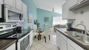 A modern kitchen with white cabinets, a black stove, and a glass dining table with chairs.