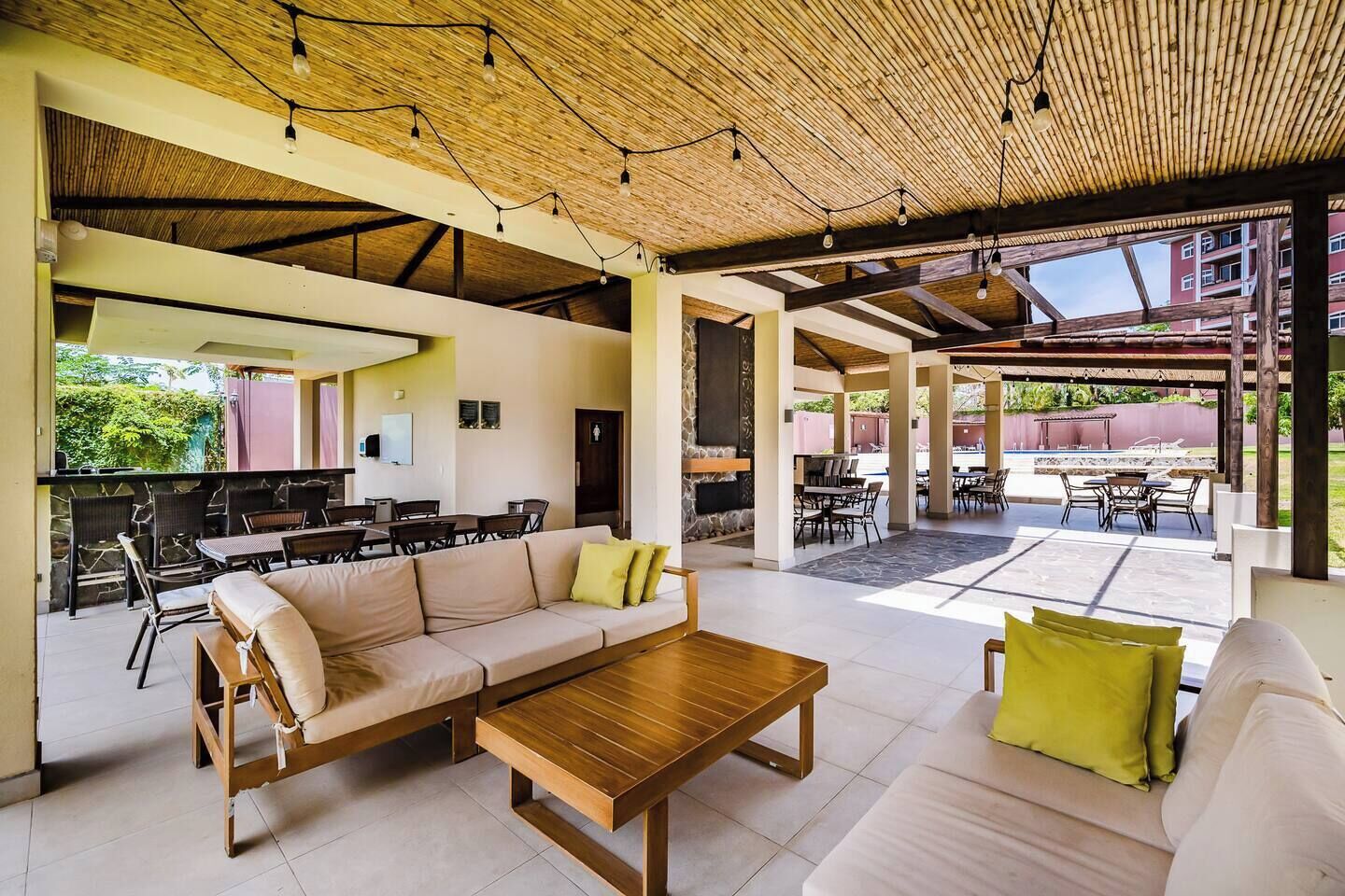 An open-plan living area with a wooden ceiling, a sofa set, a coffee table, and a dining area with chairs and a table.