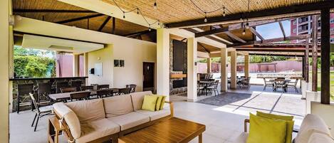 An open-plan living area with a wooden ceiling, a sofa set, a coffee table, and a dining area with chairs and a table.