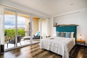 A bedroom with a large sliding glass door leading to a balcony, a bed with a teal headboard, and a small bedside table with a lamp.