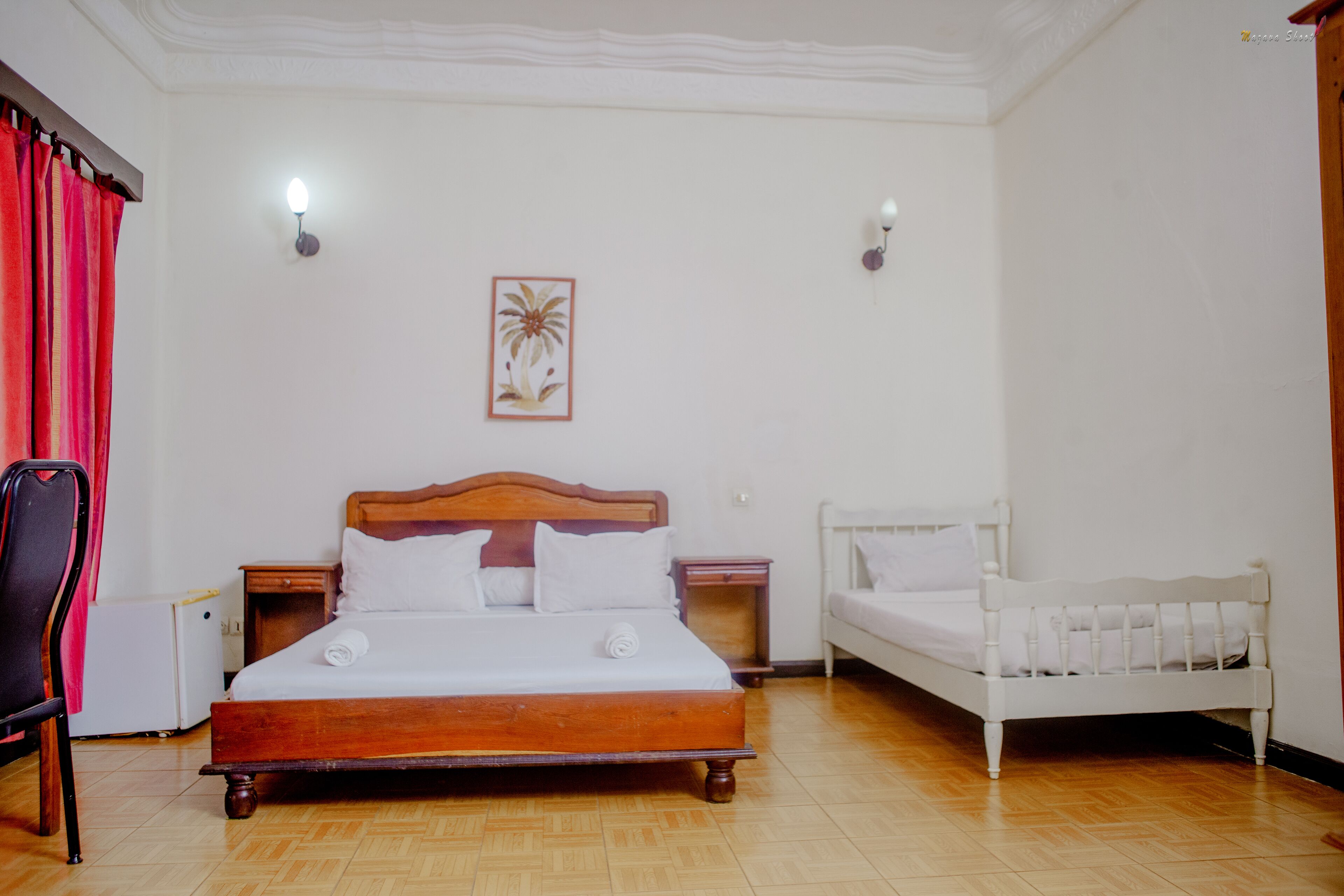 Ein Schlafzimmer mit einem hölzernen Bett, einem weißen Bett, einem Sessel, einem Nachttisch und einer Wandleuchte.