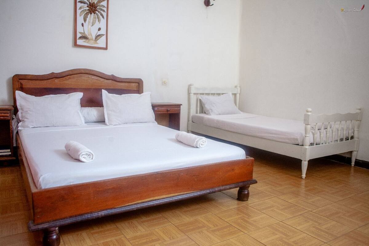 Un dormitorio con una cama de madera grande, una cama individual más pequeña y una mesita de noche con lámpara.