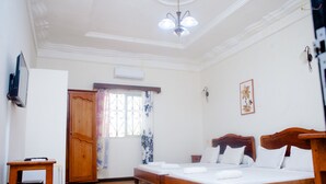 A hotel room with two wooden beds, a wooden nightstand, a small table, a television, and a window with curtains. - LOTUS HOTEL DIEGO (Antsiranana)