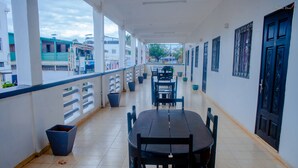 A covered balcony with a table and chairs, potted plants, and a view of the street. - LOTUS HOTEL DIEGO (Antsiranana)