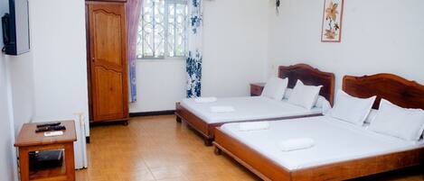 A room with two wooden beds, a wooden table, a TV, and a window with curtains.