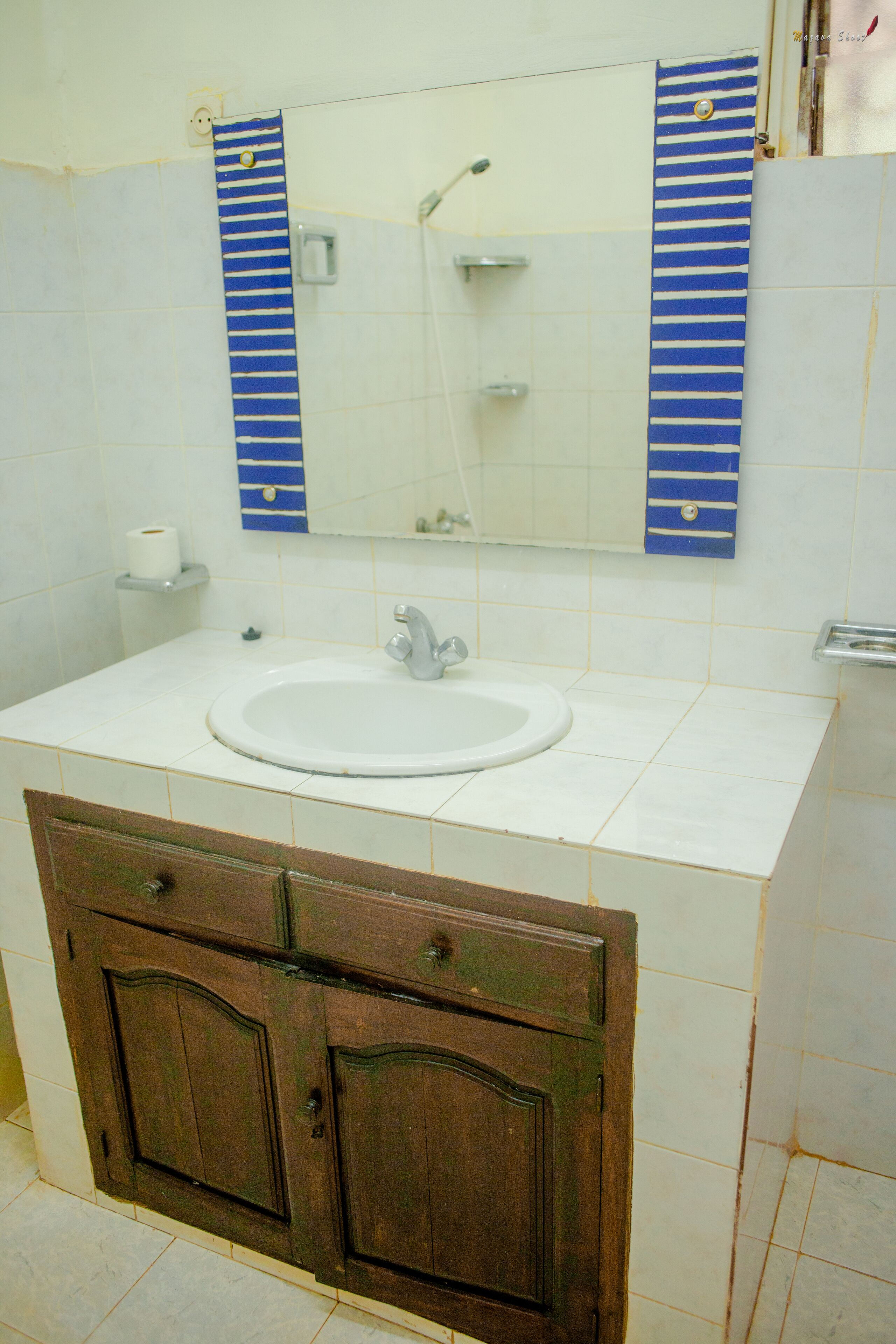 Un baño con lavamanos blanco, armarios de madera, un espejo y un perchero rayado.