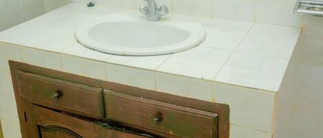 Un baño con lavamanos blanco, armarios de madera, un espejo y un perchero rayado.