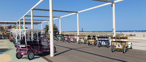 A beachside boardwalk with a row of golf carts numbered 1 to 8, a white structure with a roof, and a clear blue sky.