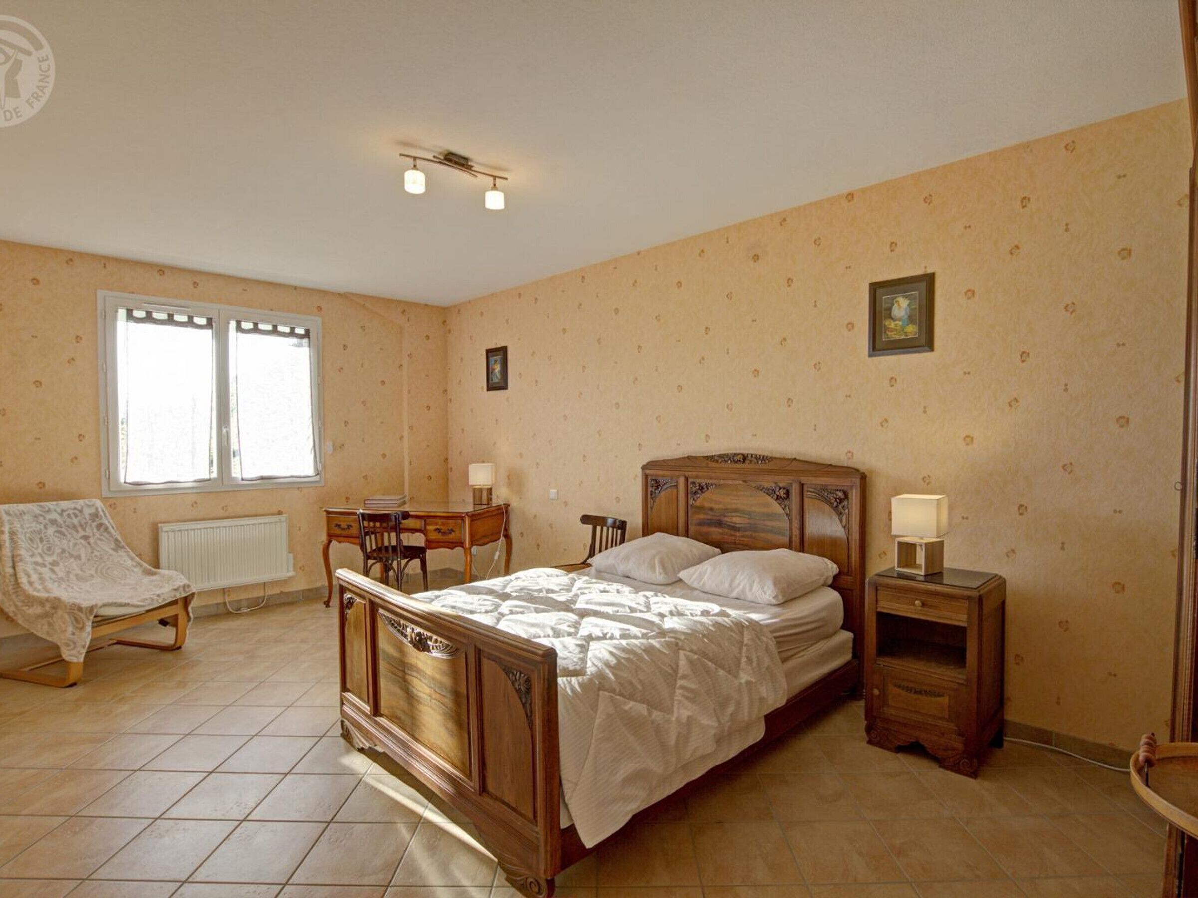 A bedroom with a wooden bed, a desk, a chair, and a radiator.