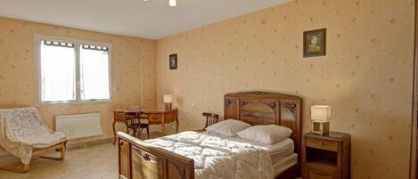 A bedroom with a wooden bed, a desk, a chair, and a radiator.