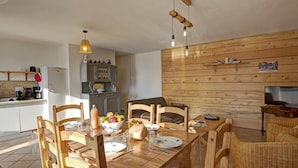 A dining area with a wooden table, chairs, and a hanging light fixture. - Rural lodge with garden and children's play area (Saint-Romain-en-Jarez)